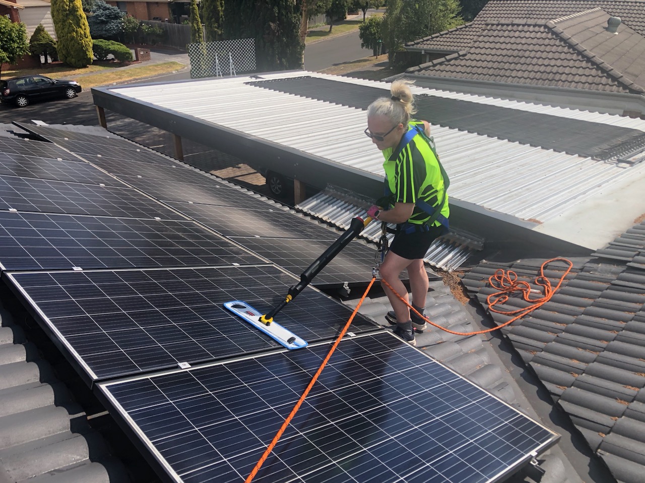 Man in high-visibility top on a roof cleaning solar panels with a mop