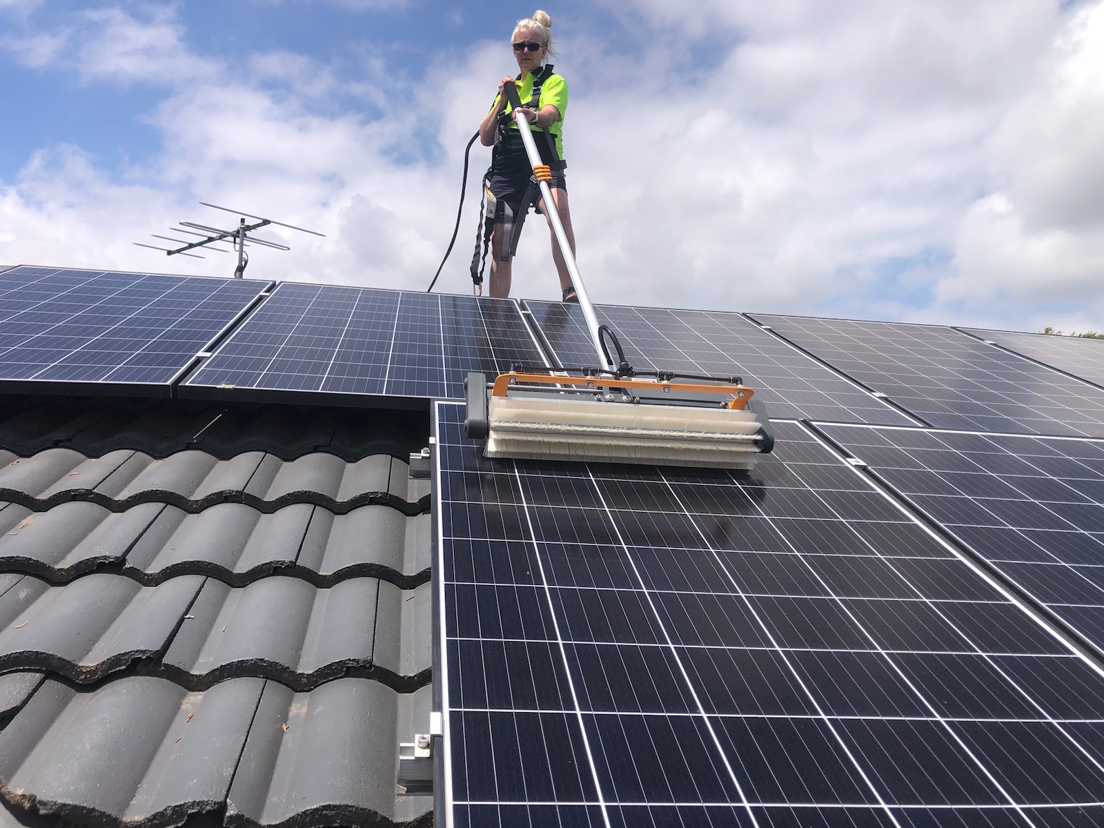 Close up photo of a specialized cleaning roller on solar panels with a woman in high visibility clothing in background